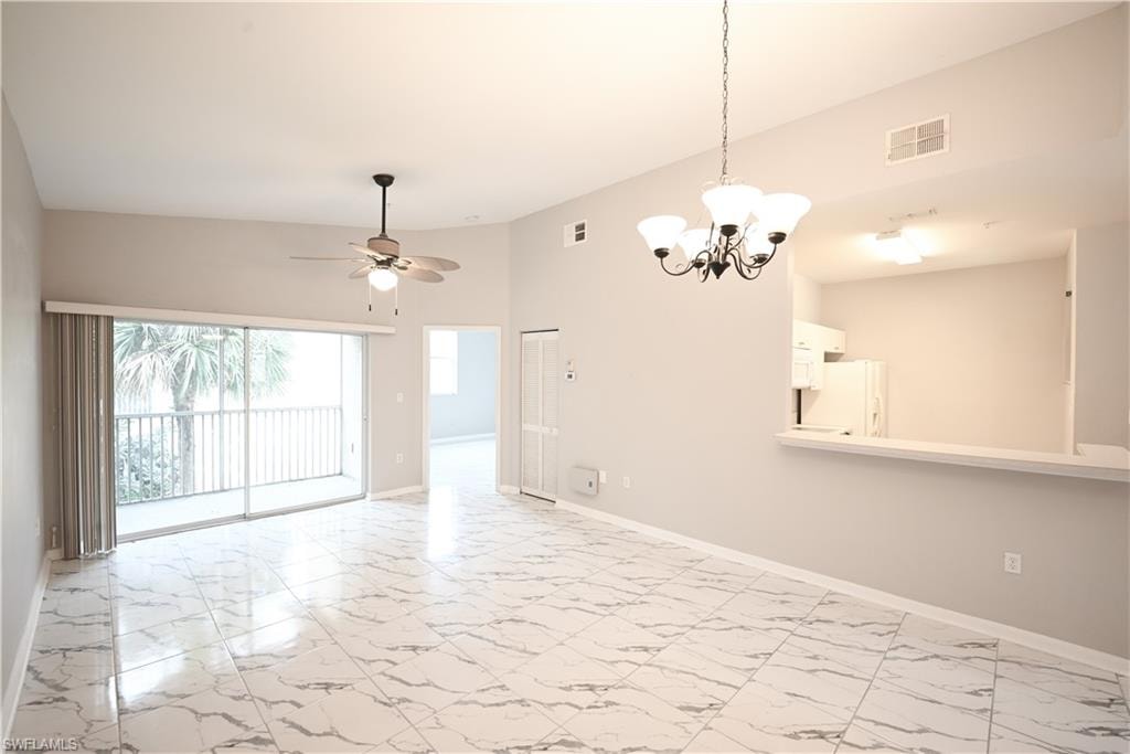 Spacious living area featuring polished tile flooring, sliding glass doors to a balcony, a ceiling fan, and a chandelier