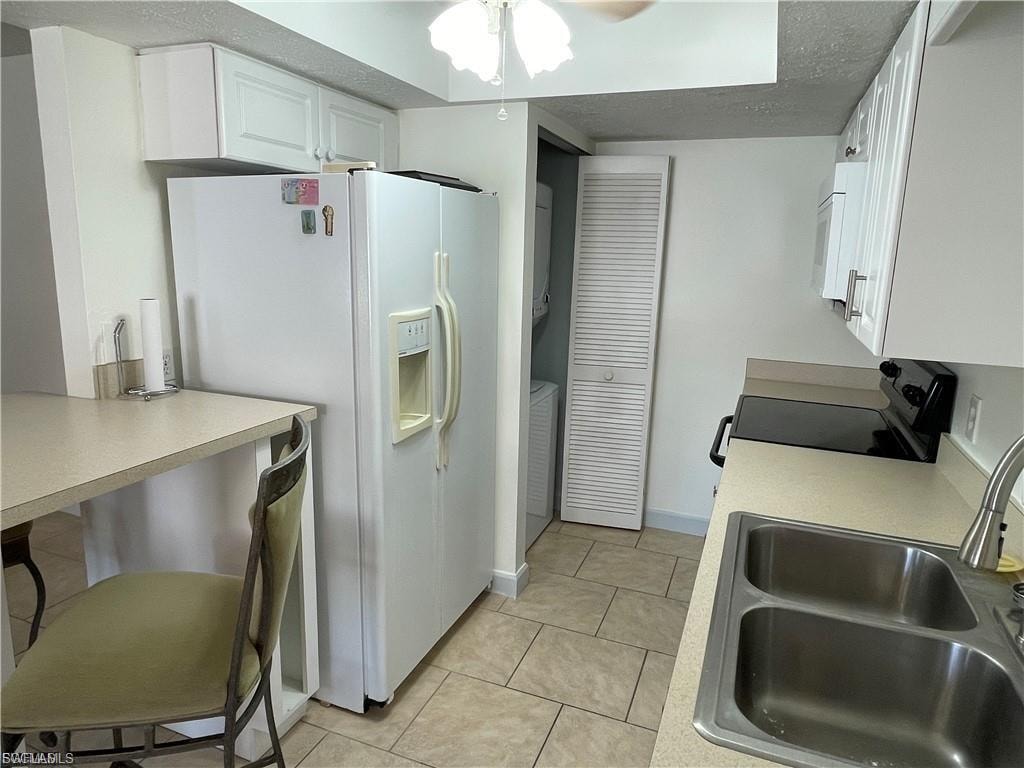 Kitchen featuring white cabinetry, light-toned countertops, a double basin stainless steel sink, and tile flooring