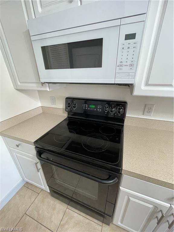 White overhead microwave, black electric range, light-toned countertops, and white cabinetry