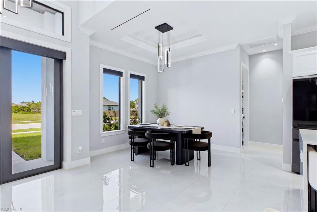 White tile flooring, recessed ceiling with crown molding, contemporary chandelier, three large windows, and a glass-paneled door