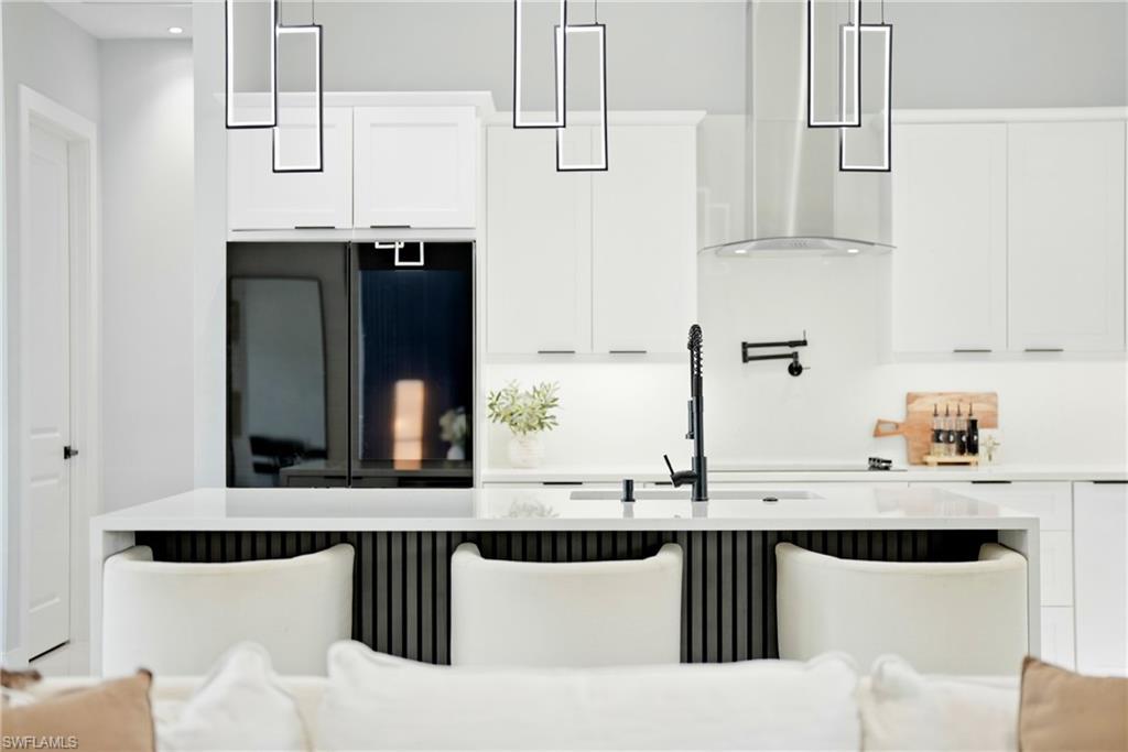 Kitchen featuring white cabinetry, a large kitchen island with counter seating, a stainless steel range hood, and modern pendant lighting