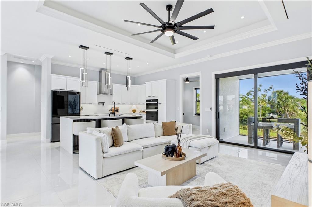 Open-concept living area featuring white tile flooring, a tray ceiling with a ceiling fan, and recessed lighting