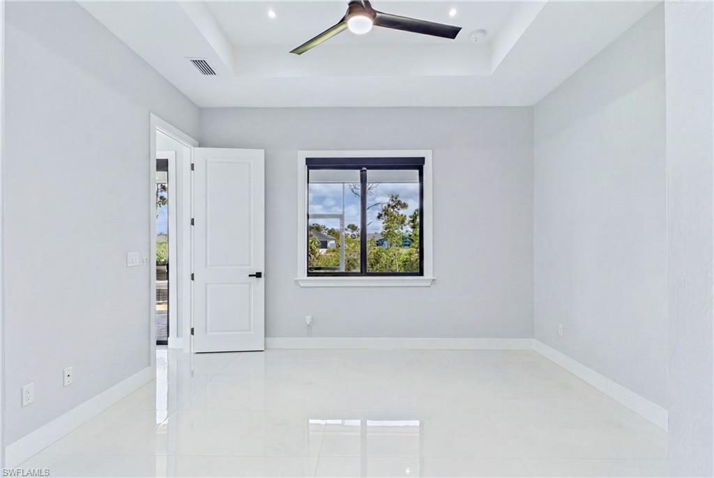 White tile flooring, tray ceiling with recessed lighting, ceiling fan, white paneled door, and a black-framed window