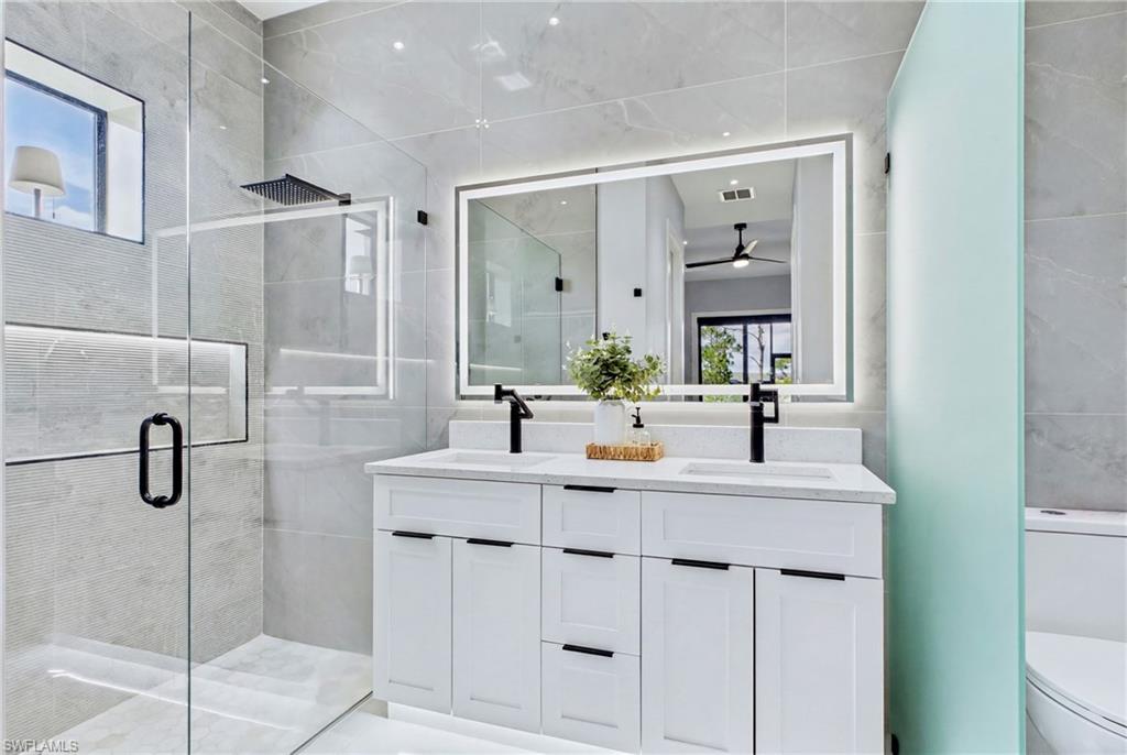 Dual vanity with white cabinetry, matte black fixtures, and an illuminated mirror