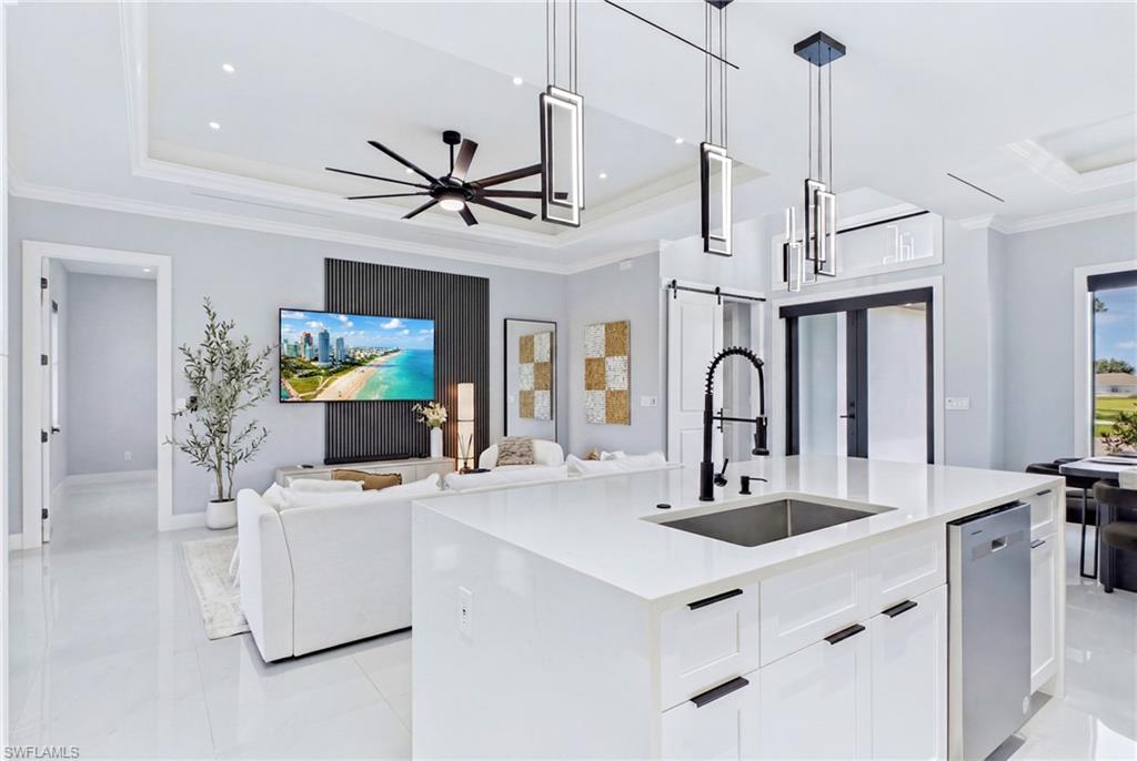 White kitchen island with an undermount sink and matte black faucet, modern pendant lighting, white cabinetry with black hardware, and a stainless steel dishwasher
