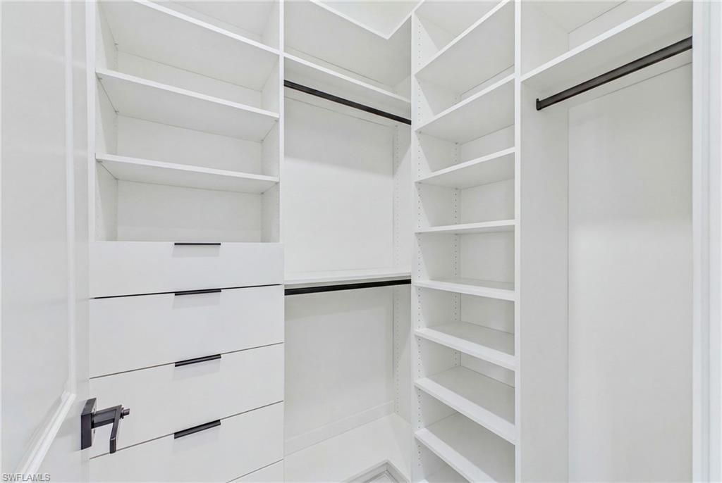 Custom white built-in closet system featuring multiple shelving units, integrated drawers with dark hardware, and hanging rods