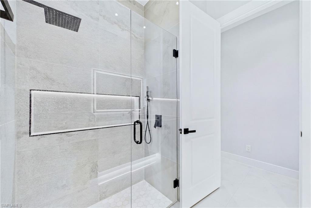 Spacious shower enclosure with glass panels, a rain shower head, built-in recessed shelving, and hexagonal floor tiling