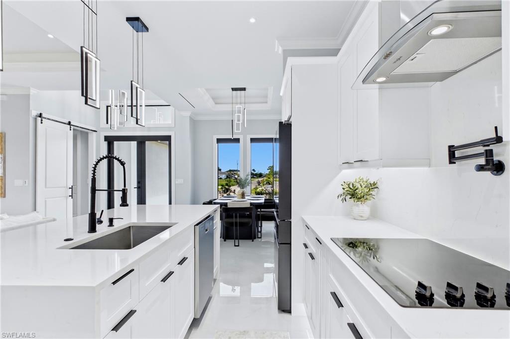 Modern kitchen featuring white cabinetry, a large center island with an undermount sink, black appliances, and a built-in cooktop with an overhead range hood