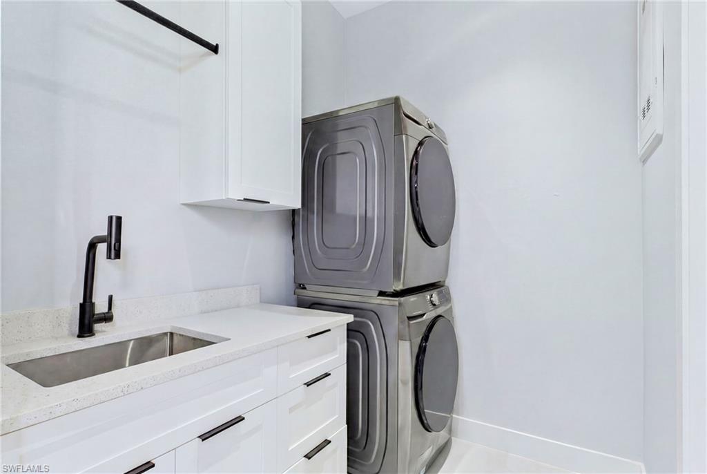 Laundry area featuring white cabinetry, a stainless steel sink, a matte black faucet, light-colored countertops, and stacked appliances