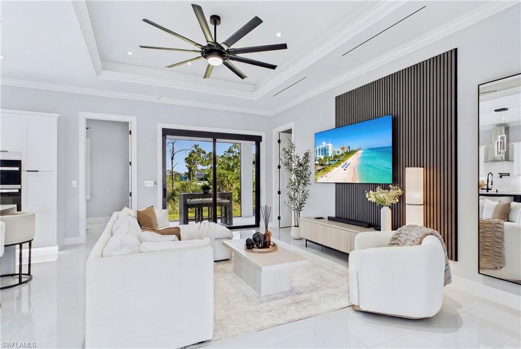 Tray ceiling with crown molding, polished tile flooring, black ceiling fan, wood slat accent wall, and sliding glass doors to outdoor dining