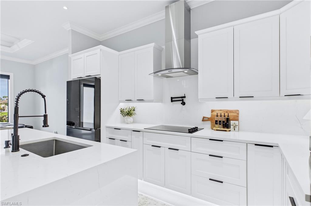 White cabinetry, stainless steel range hood, dark finish refrigerator, white countertops, and black fixtures