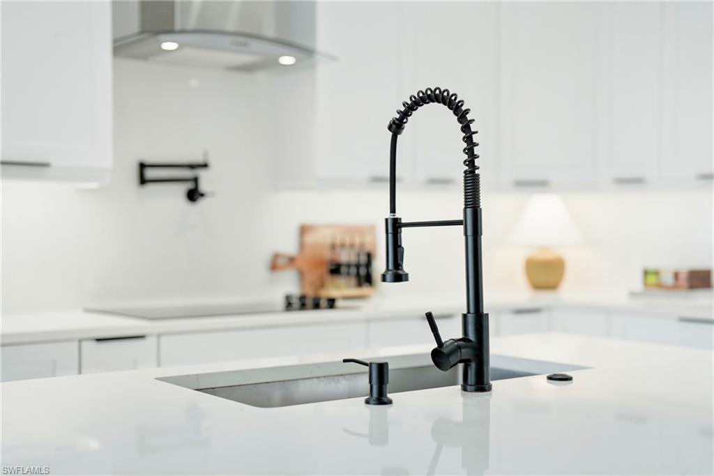 White kitchen featuring a black pull-down faucet, undermount sink, white countertops, and white cabinetry