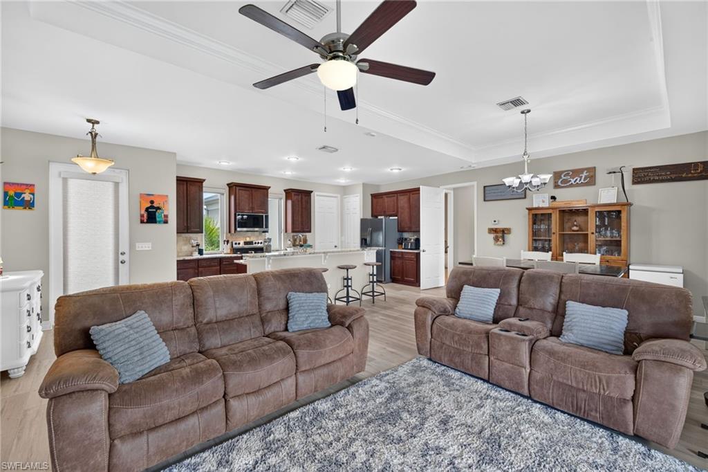 Tray ceiling with crown molding, wood-finish flooring, built-in ceiling fan, recessed lighting, and a pendant light fixture