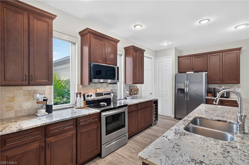 Hardwood-finish flooring, stainless steel appliances, dual basin sink, stone countertops, and dark wood cabinetry