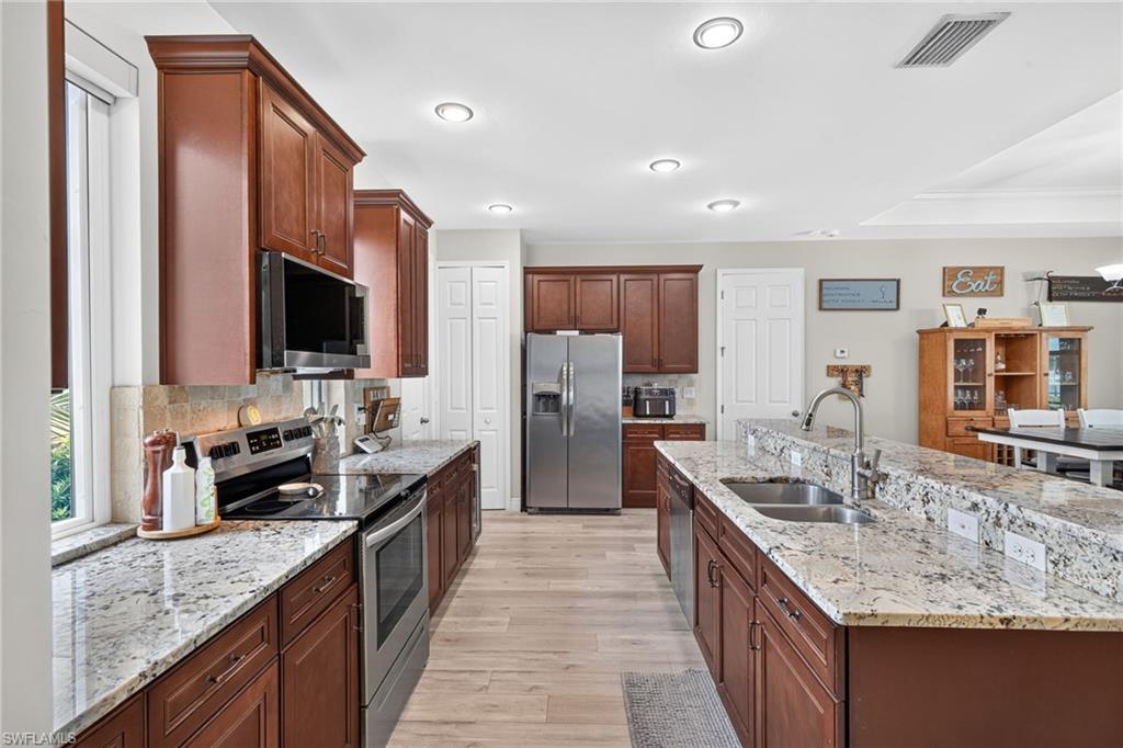 Spacious kitchen featuring extensive cabinetry, stainless steel appliances, a large center island with dual sinks, and light-toned wood-finish flooring