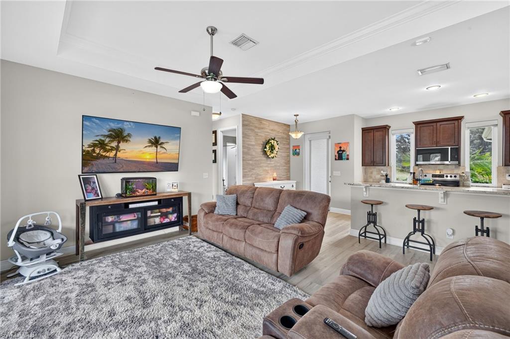 Open-concept living area featuring a tray ceiling, ceiling fan, wood-finish flooring, and a kitchen with dark wood cabinetry and a breakfast bar