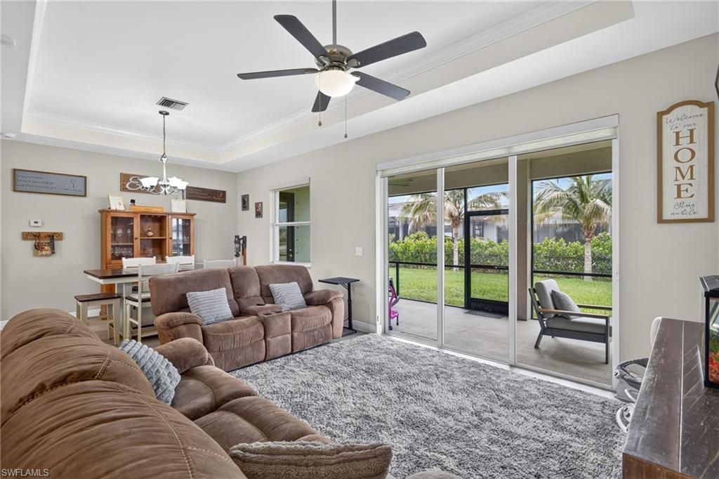 Tray ceiling with crown molding, ceiling fan with integrated lighting, sliding glass doors, screened lanai, and a landscaped backyard