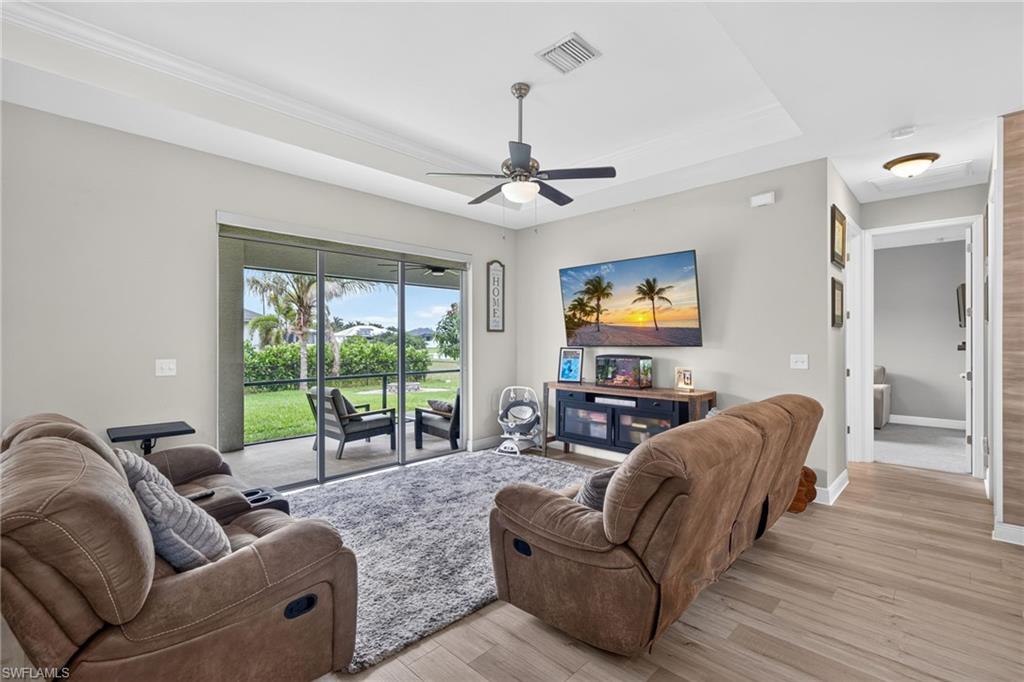 Tray ceiling with a ceiling fan, light wood-finish flooring, and sliding glass doors opening to a screened patio