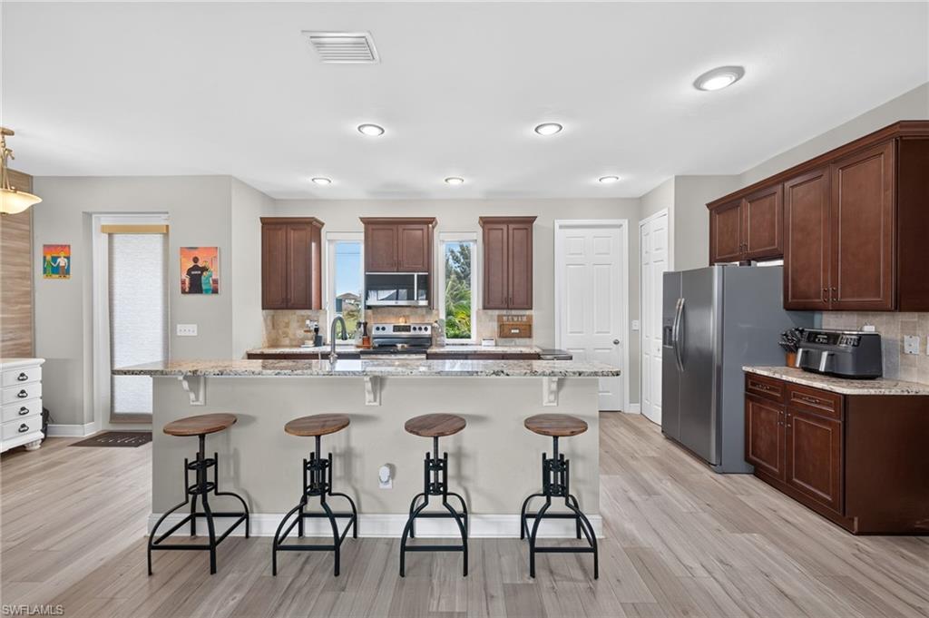 Kitchen featuring wood-finish flooring, recessed lighting, a built-in kitchen island with a stone countertop, dark wood cabinetry, and stainless steel appliances