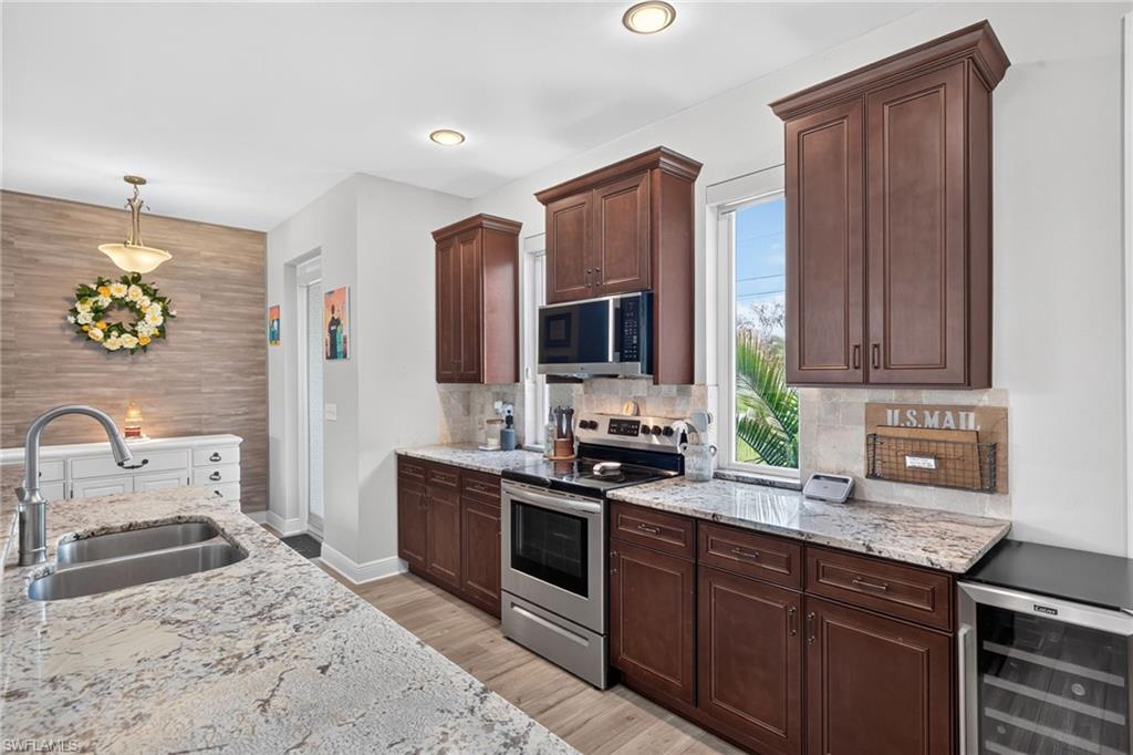 Kitchen featuring granite countertops, wood-finish flooring, stainless steel appliances, dark wood cabinetry, and a beverage cooler