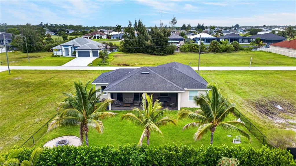 Expansive rear yard with a manicured lawn, established palm trees, and a built-in fire pit
