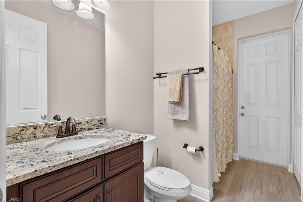 Vanity with integrated sink, stone countertop, wood-finish cabinetry, and contemporary bronze faucet