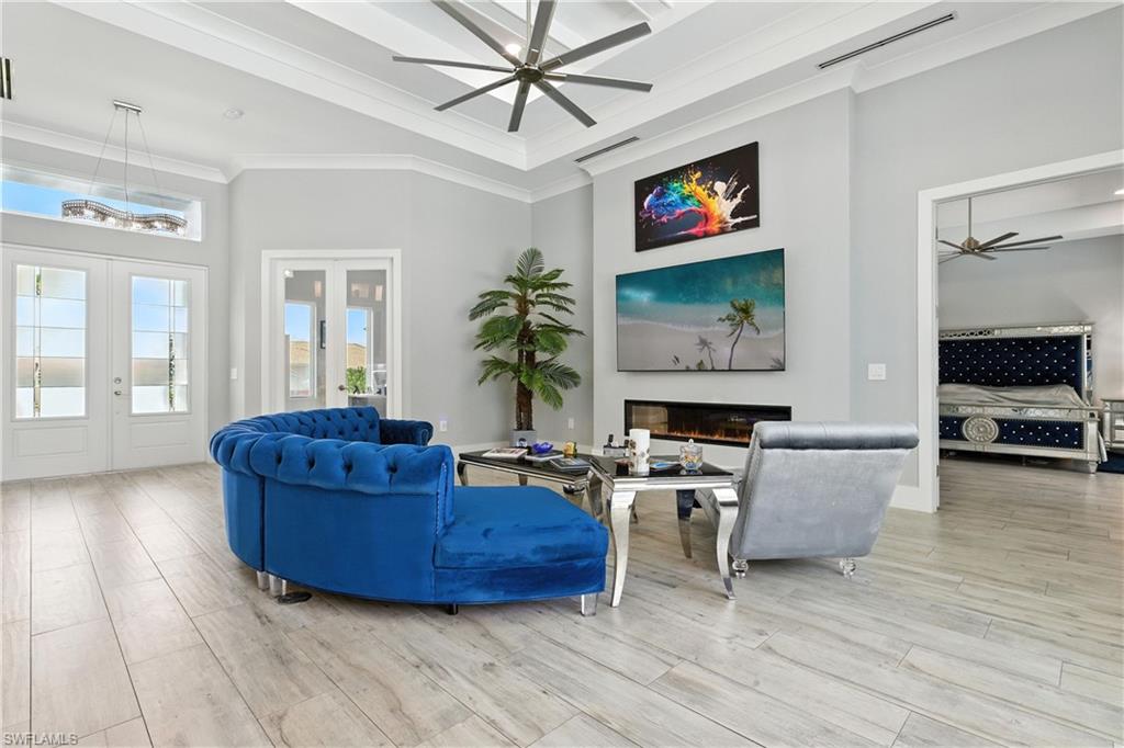 Living area with french doors, a ceiling fan, a high ceiling, crown molding, and a glass covered fireplace