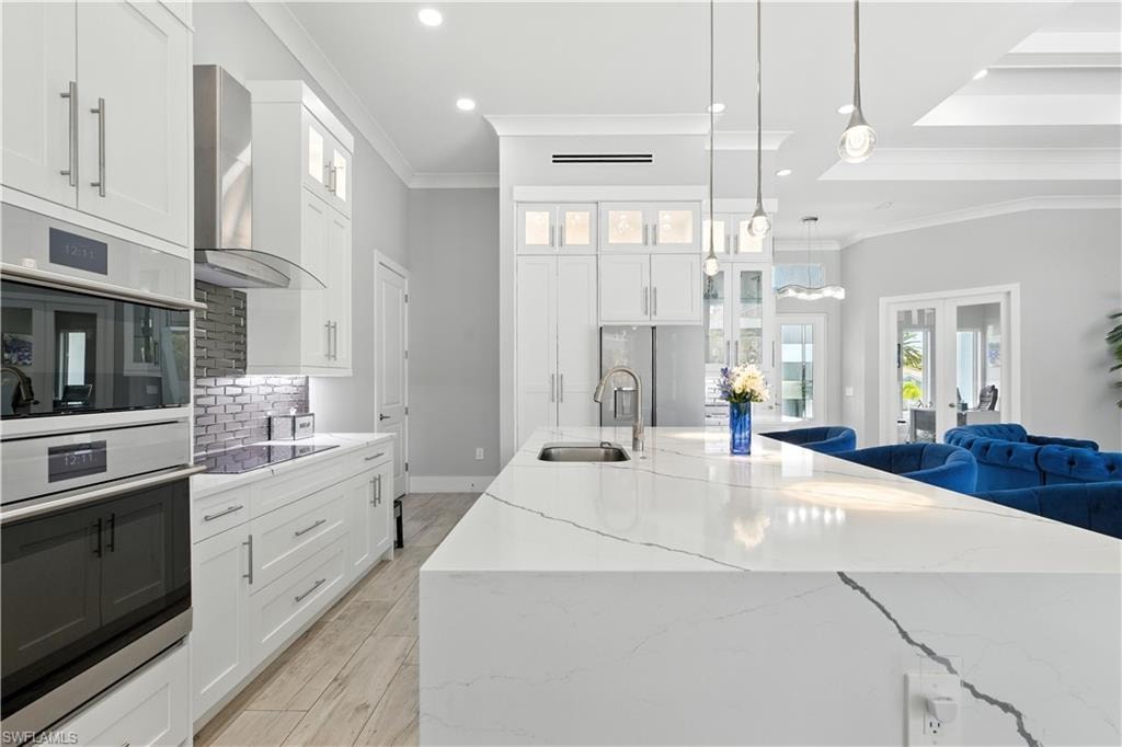 Kitchen with wall chimney range hood, crown molding, appliances with stainless steel finishes, decorative backsplash, and light stone countertops