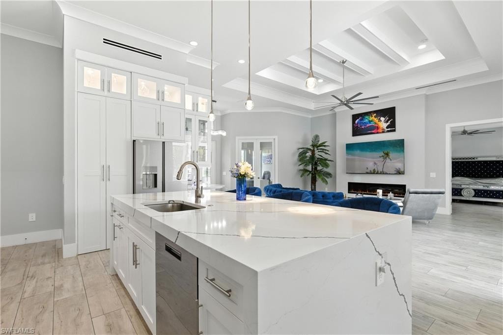 Kitchen with dishwasher, a ceiling fan, ornamental molding, a center island with sink, and light stone counters