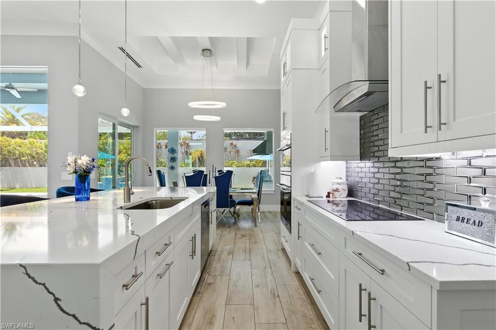 Kitchen featuring wall chimney exhaust hood, white cabinets, backsplash, light wood-style floors, and ornamental molding
