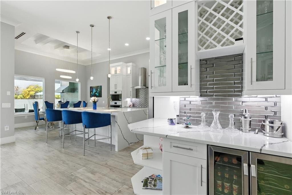 Bar area featuring backsplash, wall chimney range hood, pendant lighting, ornamental molding, and wine cooler