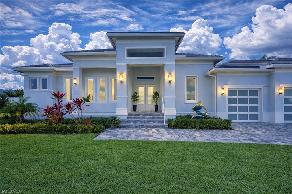Prairie-style home with a porch, a front yard, an attached garage, stucco siding, and driveway