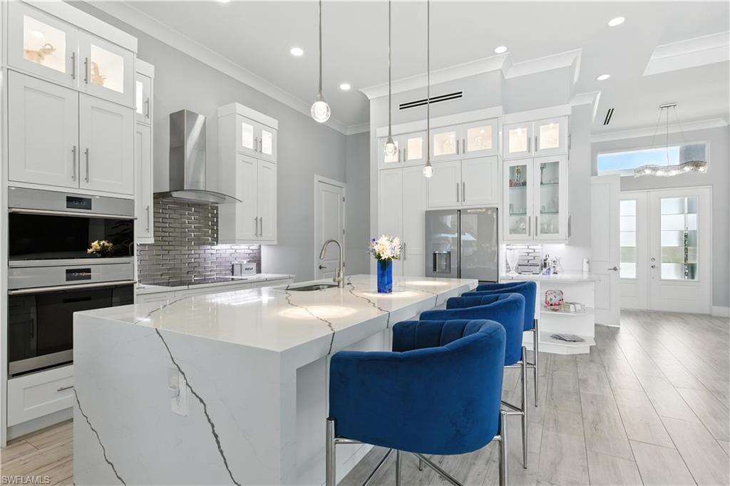 Kitchen with wall chimney range hood, appliances with stainless steel finishes, ornamental molding, tasteful backsplash, and an island with sink