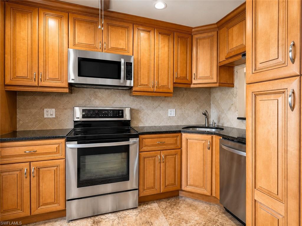 Wood-finish cabinetry with crown molding, stainless steel appliances, dark stone countertops, diamond-patterned tile backsplash, and light-toned floor tiling