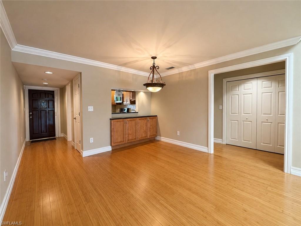Crown molding detail, wood-finish flooring, built-in cabinetry with dark countertop, overhead decorative light fixture, and a pass-through window opening