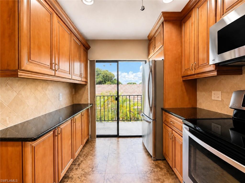Kitchen featuring wood cabinetry, dark countertops, tiled backsplash, stainless steel appliances, and a sliding glass door
