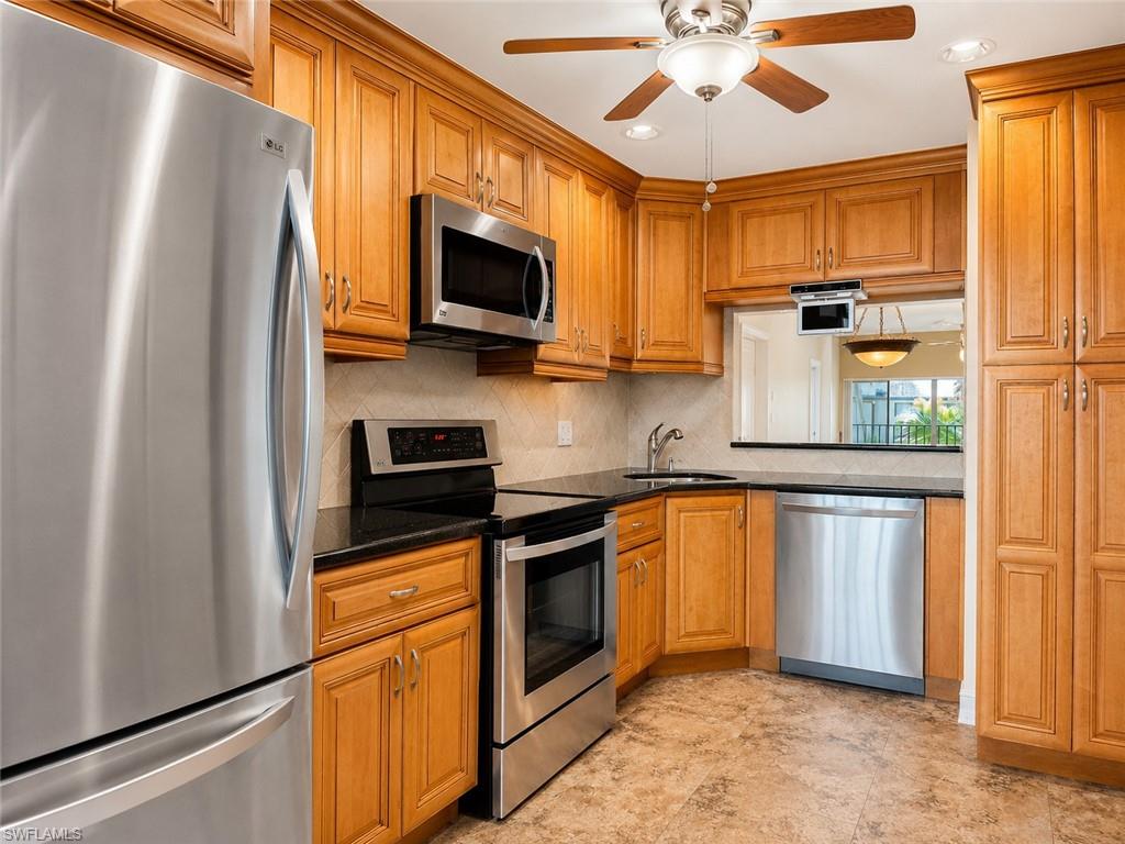 Stainless steel appliance suite, wood cabinetry, dark countertops, tiled backsplash, and wood-finish flooring