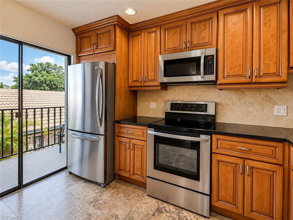 Wood-finish cabinetry, stainless steel appliances, black countertops, tile backsplash, and tile flooring