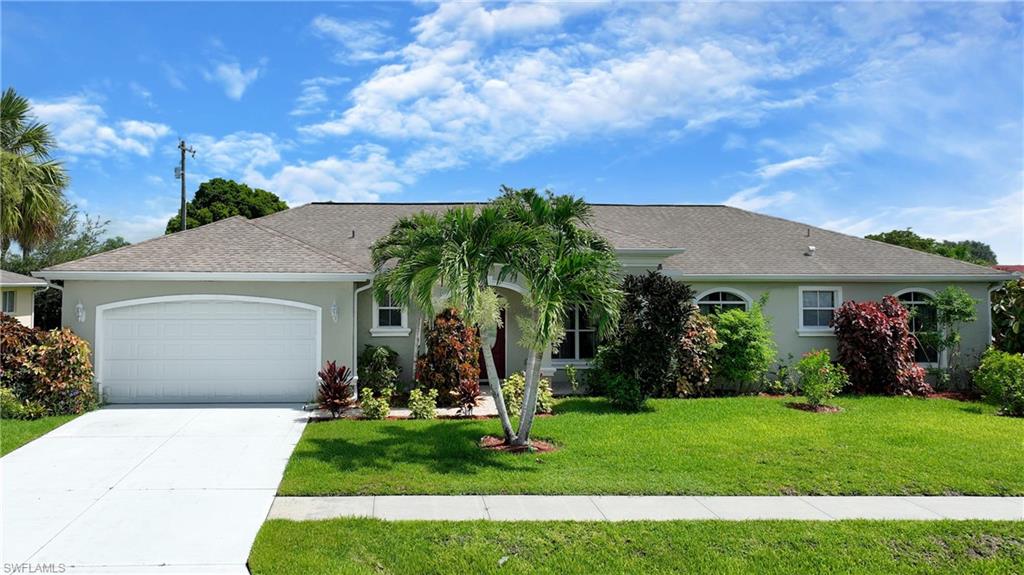 Siding exterior with a neutral paint finish, attached garage with an arched door, concrete driveway, and established landscaping including palm trees and manicured lawn