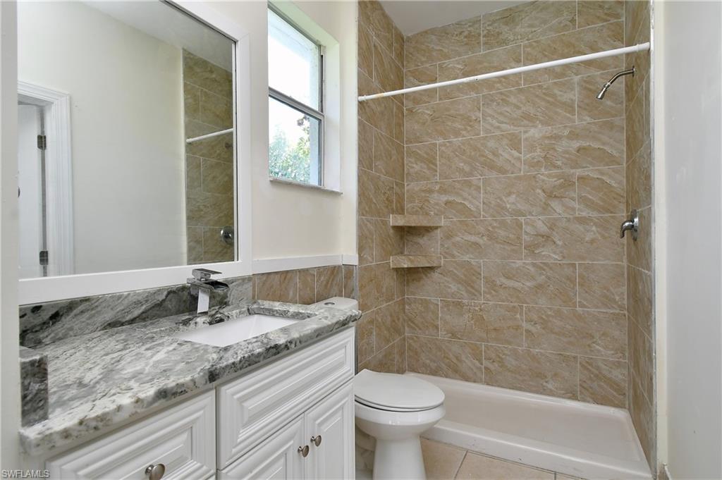 Bathroom featuring a white vanity with a light-colored countertop, an integrated sink, a chrome faucet, and a shower with tiled walls and built-in shelving