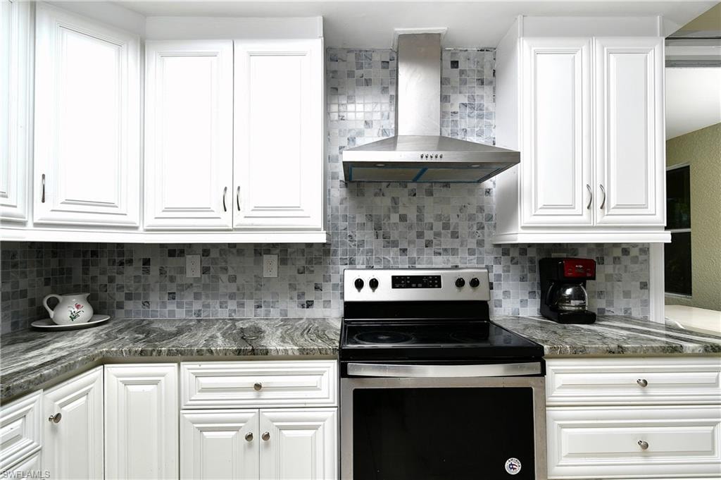 White cabinetry with decorative trim, mosaic tile backsplash, stainless steel range hood, and stone countertops