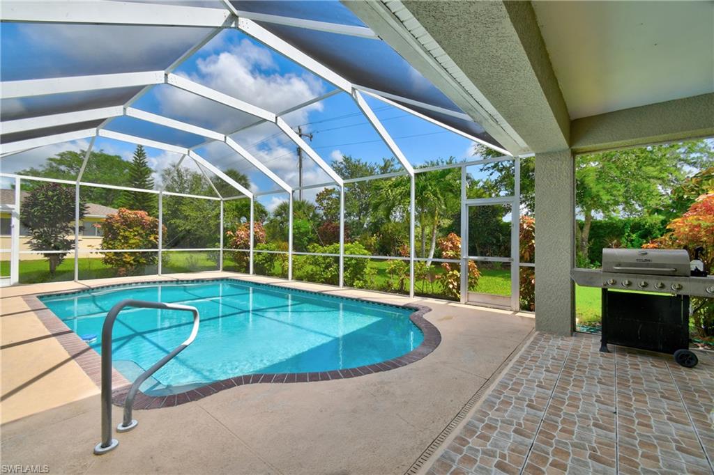 Screened lanai with curved saltwater pool featuring integrated lounge seating, brick paver decking, and panoramic views of manicured grounds and mature landscaping