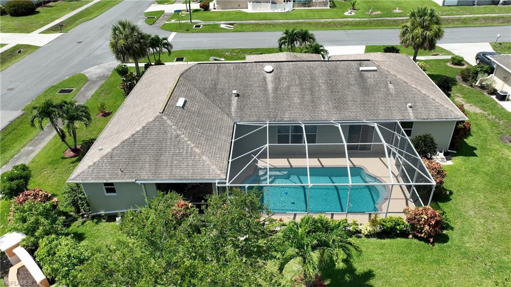 Screened-in swimming pool with a paved deck, surrounded by mature landscaping and a well-maintained lawn