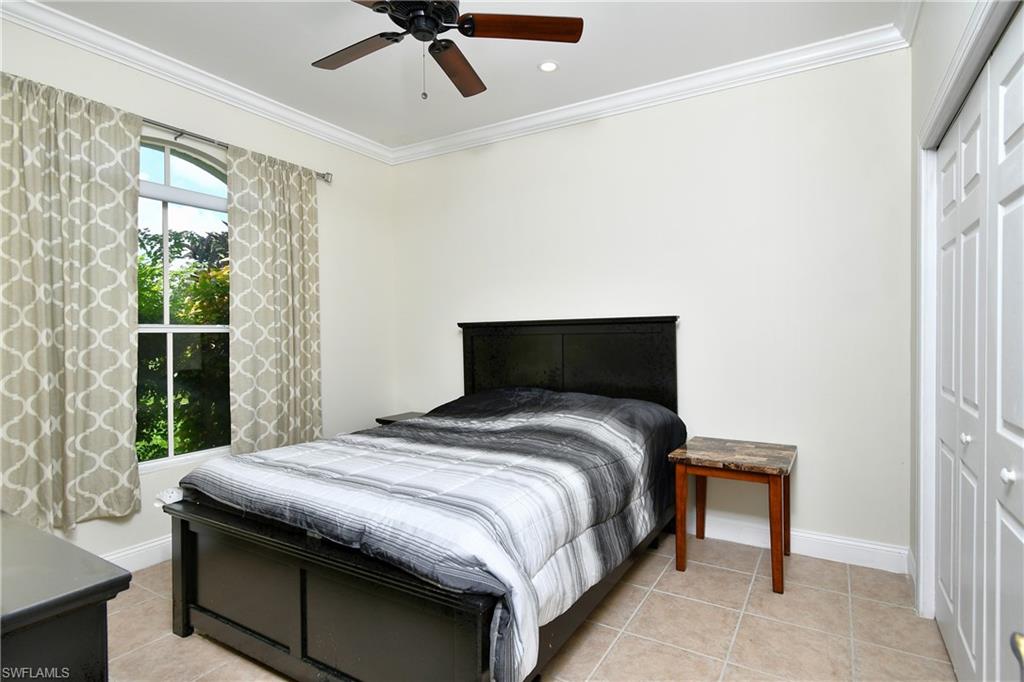 Arched window with exterior greenery, crown molding, ceiling fan, and bi-fold closet doors