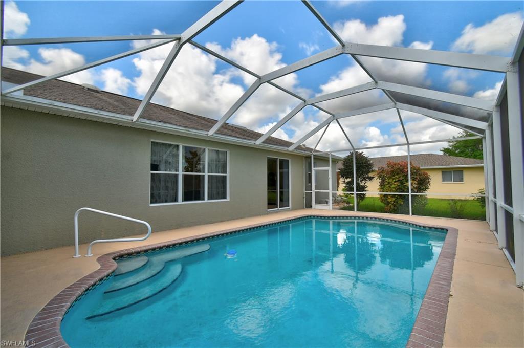 Screened-in swimming pool with integrated steps, handrail, and surrounding concrete patio
