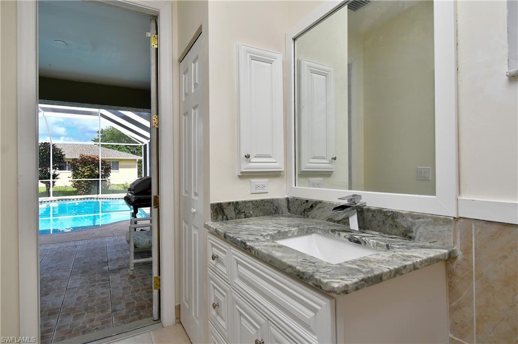 White vanity with paneled doors, stone countertop, undermount sink, and a framed mirror