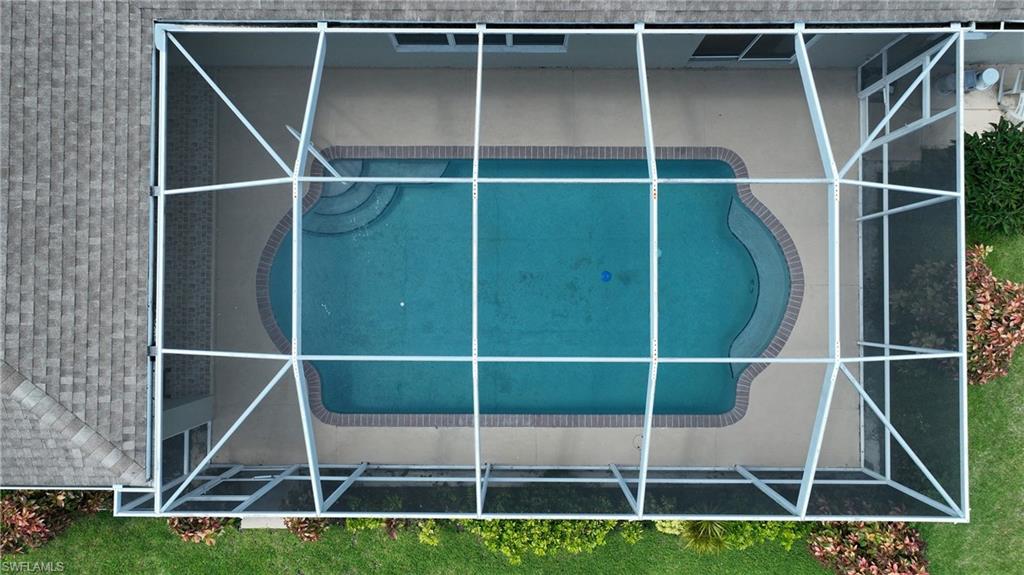 Screened enclosure featuring a swimming pool, concrete deck, and brick coping