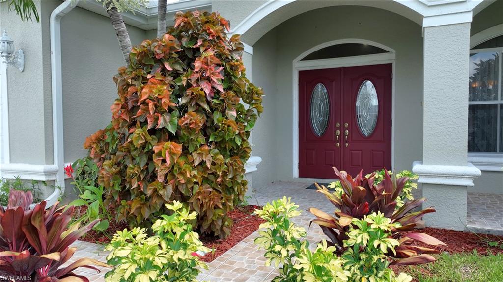 Arched entryway with double red doors featuring oval etched glass inserts, decorative exterior wall sconce, and a tiled walkway