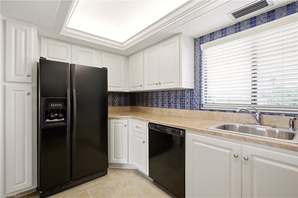Kitchen featuring white shaker cabinetry, patterned blue tile backsplash, light-toned countertops, and a black side-by-side refrigerator