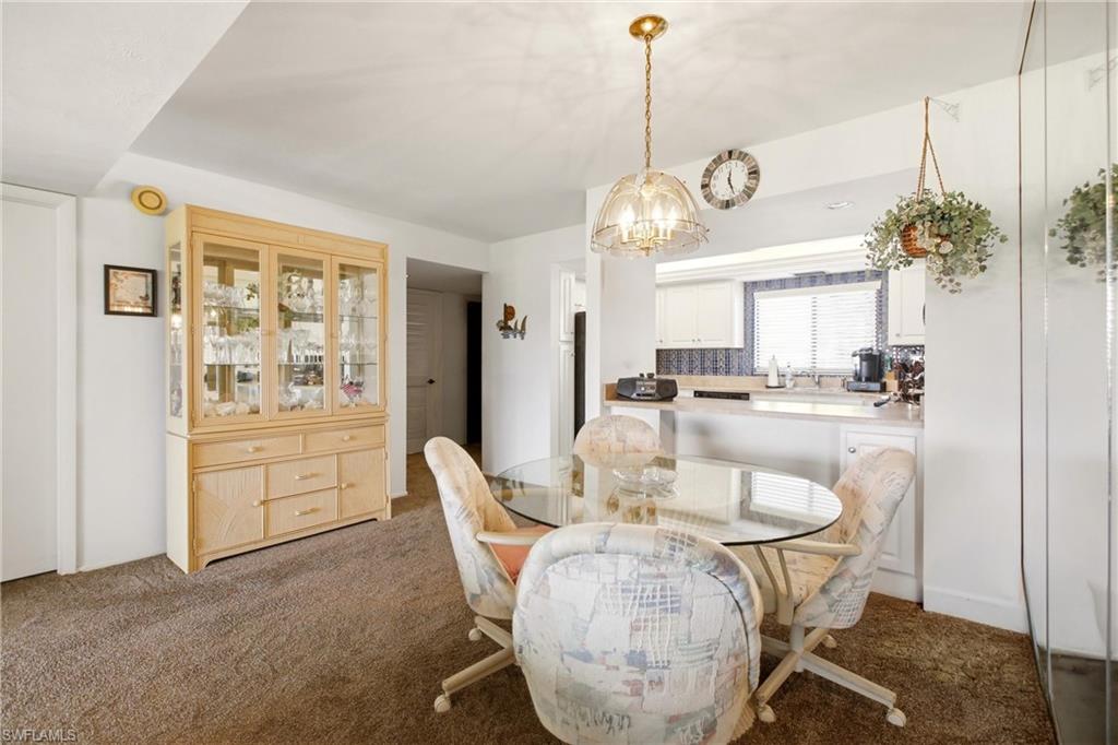 Dining area featuring a brass-tone chandelier, wall-to-wall carpeting, and a built-in display cabinet with glass doors